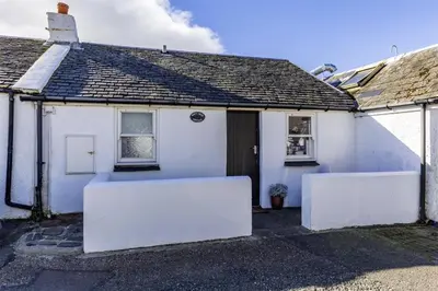 a white house with two white walls and a door at Misty Isles Cottage- Ellenabeich, Easdale, Isle of Seil