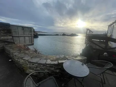 a table and chairs sitting next to a body of water at Misty Isles Cottage- Ellenabeich, Easdale, Isle of Seil
