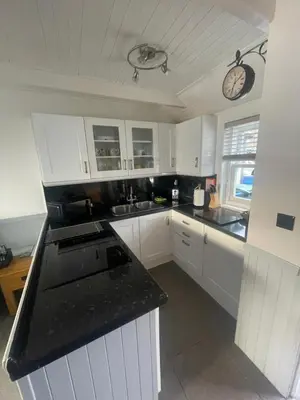 a kitchen with white cabinets and a clock on the wall at Misty Isles Cottage- Ellenabeich, Easdale, Isle of Seil