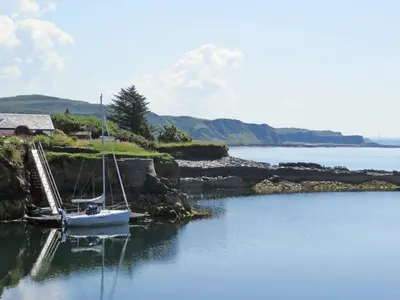 a boat is docked in a body of water at Misty Isles Cottage- Ellenabeich, Easdale, Isle of Seil
