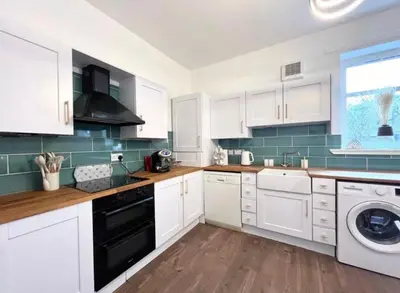 a kitchen with white cabinets and a black dishwasher at Cosy Hideaway in Stirling