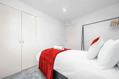 a white bedroom with a red blanket on a bed at The Elphin Escape in East Kilbride