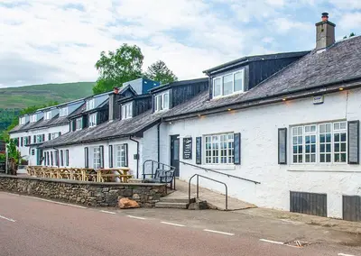 a row of white buildings with tables and benches at The Clachan Hotel, Lochearnhead in Lochearnhead