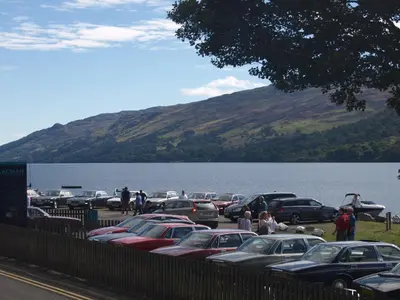 a parking lot with cars parked next to a lake at The Clachan Hotel, Lochearnhead in Lochearnhead