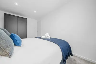 a white bedroom with a bed with blue pillows at Linden House in Hamilton