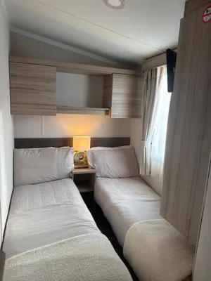a room with two beds and a table with a lamp at Luxury Seafront 3 Bedroom Caravan in Minishant