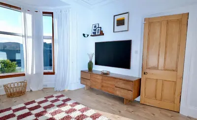 a living room with a television and a wooden door at Carmona Bank in Dunoon
