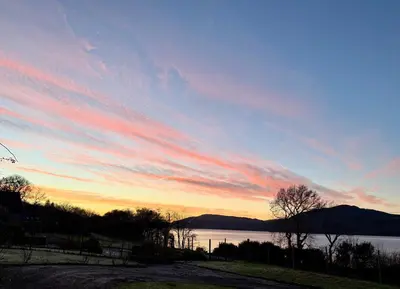 a sunset over a body of water with a sky at Oaktree Cottage, overlooking Loch Fyne in Cairndow
