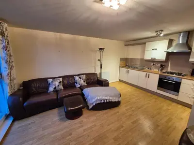 a living room with a brown couch and a kitchen at Glasgow Southside Apartment in Glasgow