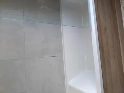 a glass shower door in a bathroom with white tiles at A room in a house in Moffat