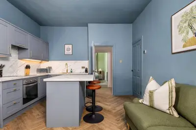 a kitchen with blue walls and a couch and a table at Modern 1-Bed Retreat by Stirling Train Station in Stirling
