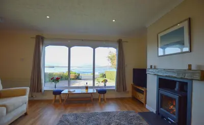 a living room with a fireplace and a large window at An Cala in Connel