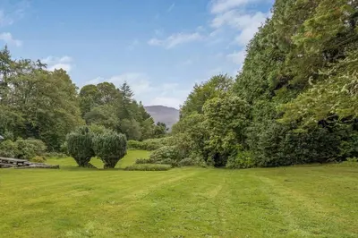 a grassy field with trees and a hill in the background at Finest Retreats - Garden Cottage at Ormidale House in Clachan of Glendaruel