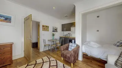 a bedroom with a bed and a chair and a kitchen at Finest Retreats - Garden Cottage at Ormidale House in Clachan of Glendaruel