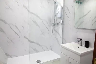 a white bathroom with a shower and a sink at Vacant Nests Ivy Cottage 3BR Wi-Fi in Kilsyth