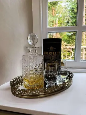 a bottle of whiskey and two glasses on a tray at Burn Cottage - A Secluded Highland Retreat For Two in Fortingall