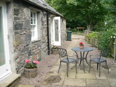 a table and chairs in front of a stone house at Burn Cottage - A Secluded Highland Retreat For Two in Fortingall