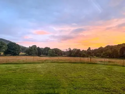 a field with a fence and a sunset in the background at Riverview Lodge in Acharra