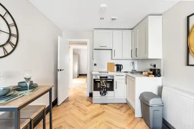 a kitchen with white cabinets and a dining table at Newly Renovated 1BR Steps from Hove Beach in Moffat