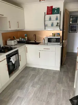 a kitchen with white cabinets and wooden floors at The Bonnie Stay Garden Apartment in Largs