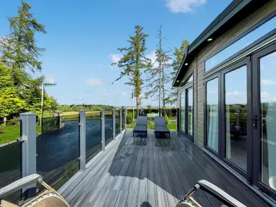 a house with a deck with chairs on the water at Woodland View in Auchterarder