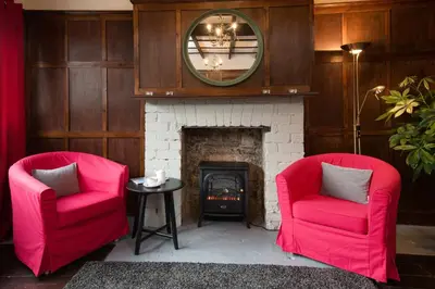 two red chairs in a living room with a fireplace at Glenbruar House in Crianlarich