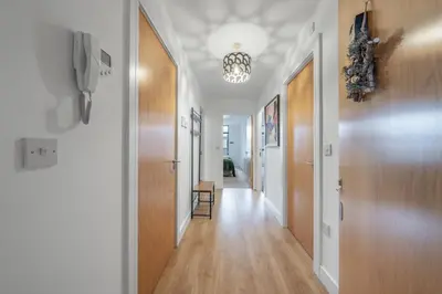 a hallway with white walls and wood floors and a chandelier at Modern 2-Bed Flat with Balcony and Free Parking - Ideal for Contractors in Moffat