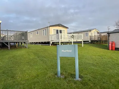 a sign in the grass in front of a row of houses at Home from Home at the Hendersons Caravan in Kilwinning