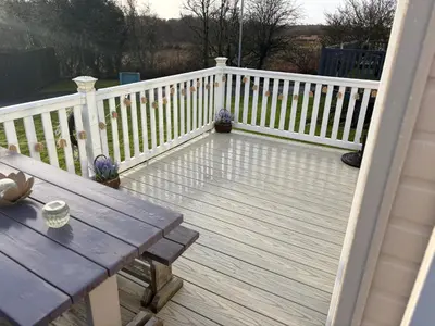 a wooden deck with a picnic table and a fence at Home from Home at the Hendersons Caravan in Kilwinning