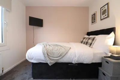 a bedroom with a bed with white sheets and a television at Modern 3BR Home with Parking in East Kilbride