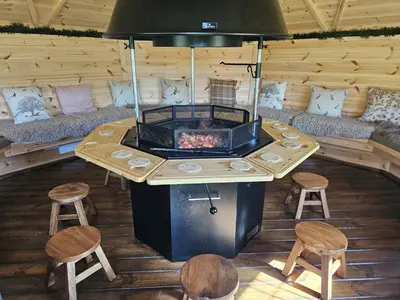 a room with a table with a fireplace and stools at Woodland Oak Log Cabin, by Meall nan Tarmachan in Killin