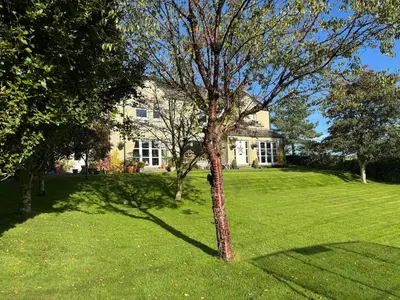 a tree in the grass in front of a house at Borders Escape with Hot Tub in West Linton