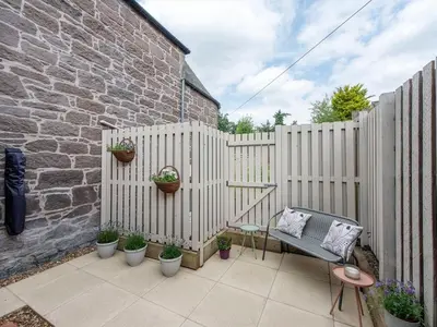 a patio with a fence with potted plants and a chair at Meadow Hill Cottage with Private Garden, Crieff in Crieff