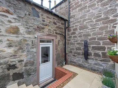 a brick building with a white door in front of it at Meadow Hill Cottage with Private Garden, Crieff in Crieff
