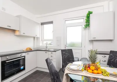 a kitchen with white cabinets and a table with fruit on it at Broomfield No 31 by Klass Living Airdrie in Airdrie
