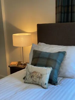 a pillow sitting on a bed next to a lamp at Keeper's Cottage at Slogarie Estate in Castle Douglas