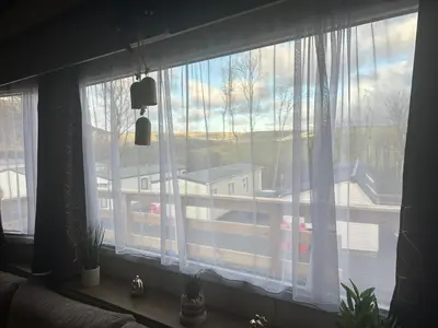 a window with white curtains and a view of a building at BZ Green Haven Caravan in Ballantrae