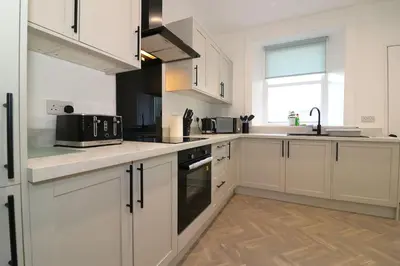 a kitchen with white cabinets and a black appliance at Modern 2 Bedroom Cottage Flat in Stenhousemuir