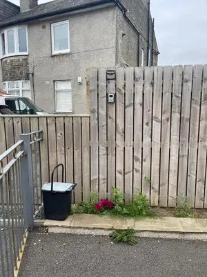 a fence with a trash can next to a house at ShekNup Home in Edinburgh