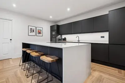 a kitchen with black and white cabinets and bar stools at Spacious 5 Bedroom Home With 3 Bathrooms And Private Parking in Glasgow