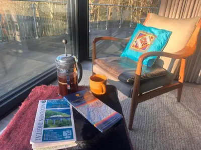 a room with a chair and a table with a book at Spacious, bright home in Central Scotland sleeps 6 in Balfron