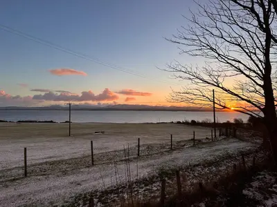 a sunset over a field with a fence and the ocean at Curlew Cottage - Peaceful Setting Stunning Views in Bruichladdich