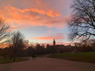 a sunset with people walking down a path in a park at Warm upgraded top-floor flat in Finnieston in Glasgow