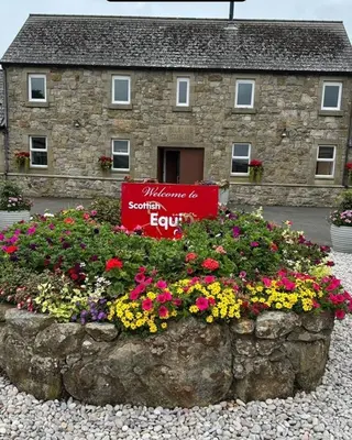 a sign in front of a stone building with flowers at Belstane Manor in Carluke