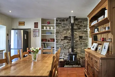 a kitchen with a wooden table and a stone fireplace at Glenalbyn Cottage in Saint Fillans