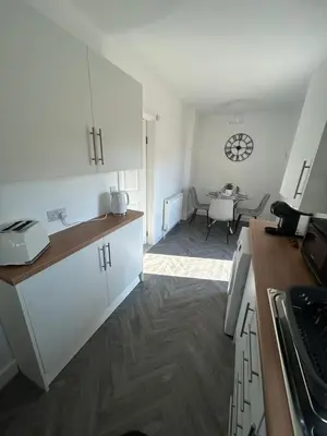 a kitchen with white cabinets and a dining room at Plains Town House, Airdrie in Caldercruix