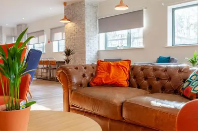 a brown leather couch with an orange pillow in a living room at Collegelands in Glasgow in Glasgow