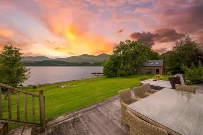 a patio with a table and a view of a lake at Ardeonaig Lodge with Hot Tub & Water Fronted Games room in Ardeonaig