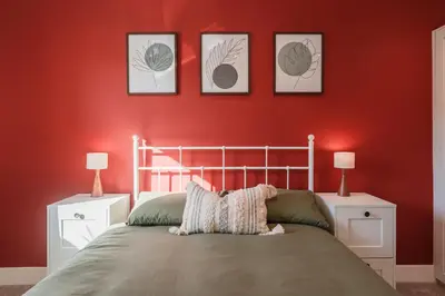 a bedroom with a red wall with a bed and three pictures at Henderson House - West End 3 Bedroom Family Home in Glasgow