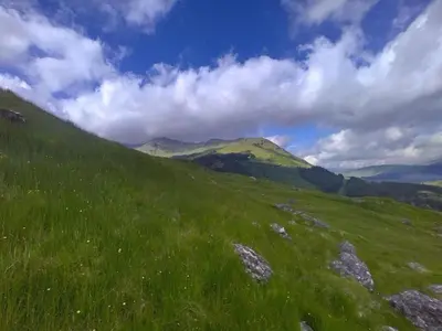 a green grassy hill with mountains in the background at Holiday Home Benmore Farm House in Stirling mit Bergblick by Interhome in Crianlarich